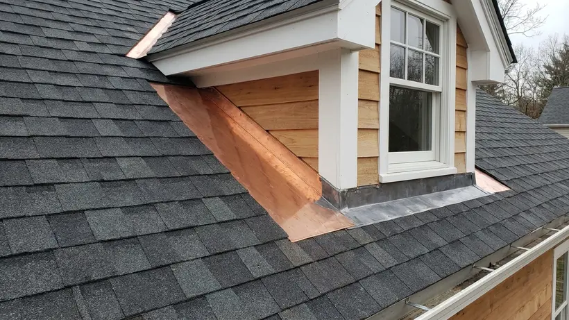 Close-up of clean shingle cuts and flashing in a roof valley near a dormer window.