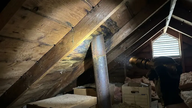 A roofing contractor inspecting attic decking for moisture and rot with a flashlight.