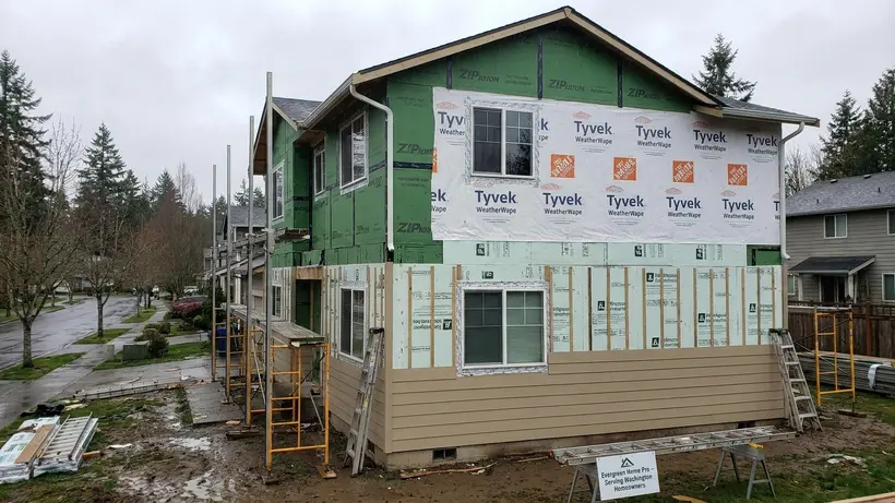 A home exterior under construction showing weather-resistant wrap and rigid foam insulation beneath new siding.